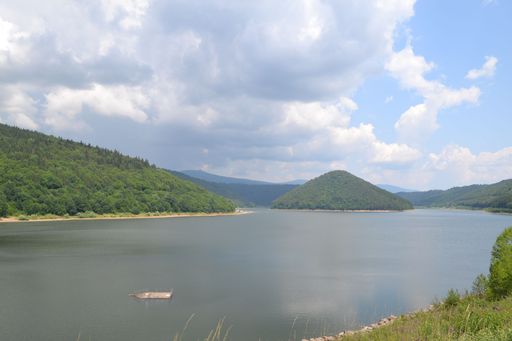 An aerial view of lake surrounded by greenery mountains under blue bright sky
