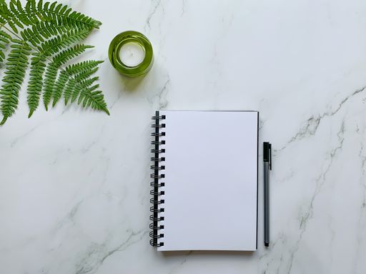 A top view of an opened notebook and pen next to decorative fern branch - perfect for wallpaper