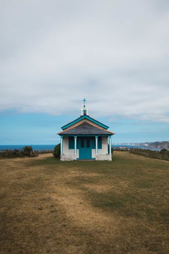 A vertical shot of the Ermita de La Regalina surrounded by the sea under a cloudy sky in Asturias, Spain