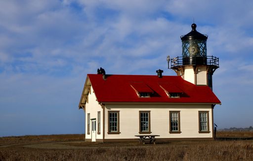 A lighthouse and a building in California against a blue cloudy sky