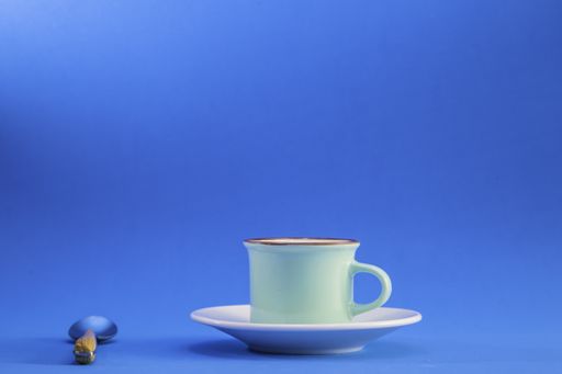 A closeup of a coffee cup with a saucer and spoon isolated on a blue background