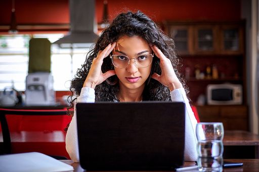 A shallow focus of a stressed Hispanic female with glasses sitting in front of her laptop