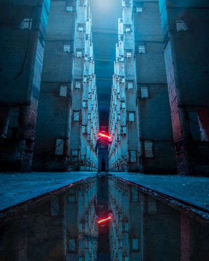A dramatic shot of a man standing in front of puddle between buildings holding red light swords