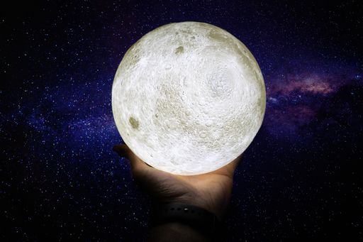 A beautiful shot of a white planet figure in a human palm with the breathtaking stellar sky in the background