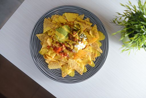 A top view of a plate of nachos with sauce on a white surface