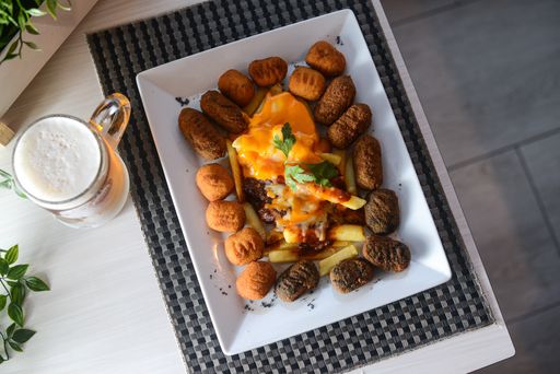 A top view of a plate of potatoes with sauce and a glass of beer on a table