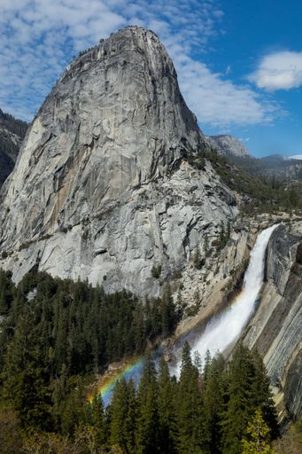 A vertical shot of Nevada Falls with a rainbow and fir trees in Yosemite National Park
