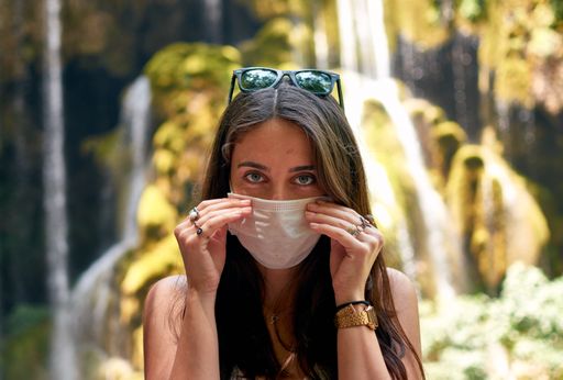 A shot of a female taking off her mask while standing near a waterfall - the new normal concept