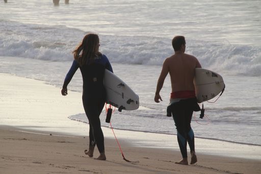 Two people dressed in wetsuits walking on a beach carrying their surfboards