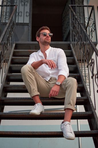 A vertical shot of a male with sunglasses sitting on the stairs