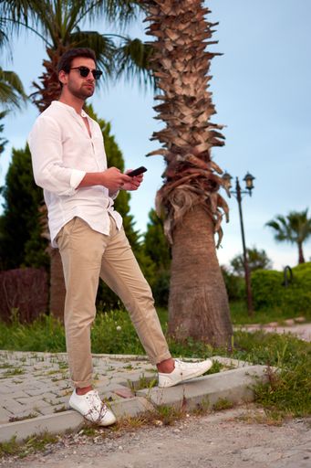 A vertical shot of a male standing confidently in a park and using his phone