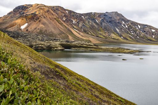 A lovely view of a calm lake surrounded by tall mountains and green fields in Iceland on a sunny day