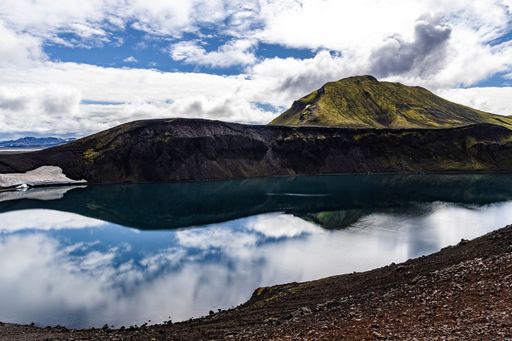 A lovely view of a calm lake surrounded by tall mountains and green fields in Iceland on a sunny day