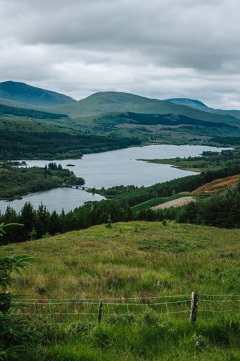 A vertical shot of a river surrounded by hills and grass on a cloudy day in Skye island, Scotland, UK