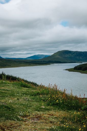 A vertical shot of a river surrounded by hills and grass on a cloudy day in Skye island, Scotland, UK