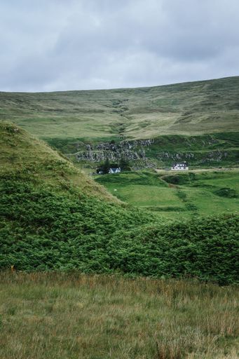 A vertical shot of a beautiful landscape of hills and mountains with houses in the background on a gloomy day