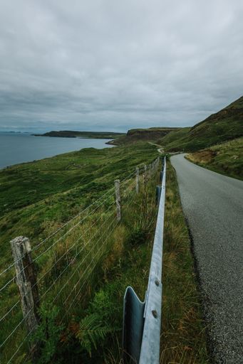 A vertical shot of from a road a lake surrounded by green landscape during a cloudy day