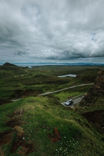 A vertical of a car driving along a trail on Skie island in Scotland captured under a grey cloudy sky