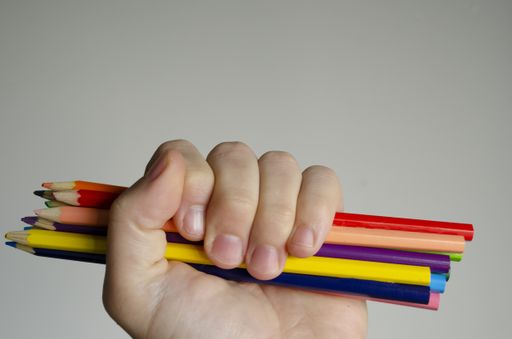 A closeup shot of a hand holding colorful pencils on a gray background