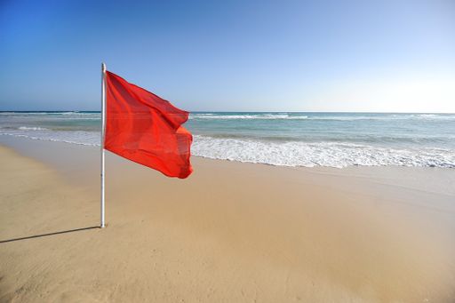 A warning sign of a red flag at a beautiful beach with a blue sky and a turquoise sea
