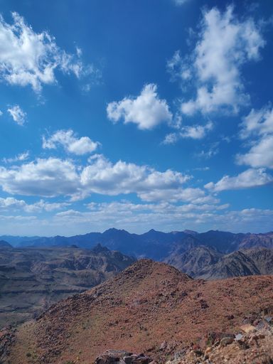 A vertical shot of a natural landscape with a desert and a mountain range under blue cloudy sky