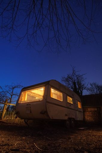 A vertical shot of an illuminated aged mobile home parked under a night sky