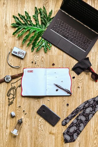 A vertical shot of a laptop, a planner, mobile phone and other accessories on a wooden surface
