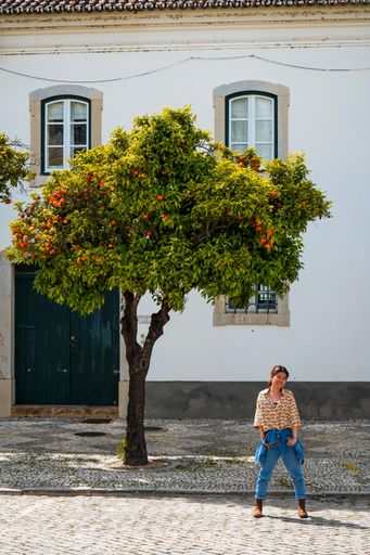 Asian woman standing in front of lush orange tree in old town Faro