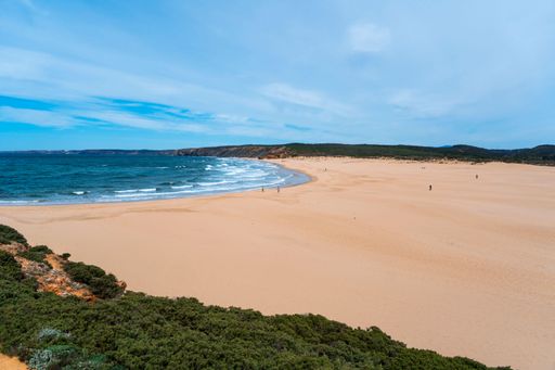 Scenic surf beach Praia da Bordeira with strong waves rolling in at Algarve Coast with lush green plants around and wide sand dunes