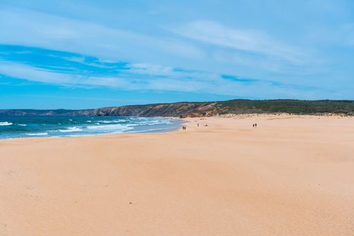 Scenic surf beach Praia da Bordeira with strong waves rolling in at Algarve Coast with lush green plants around and wide sand dunes