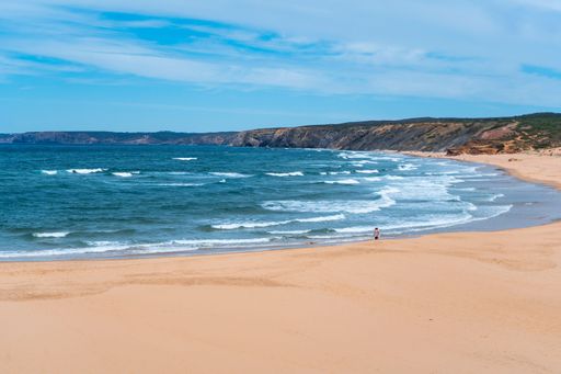 Scenic surf beach Praia da Bordeira with strong waves rolling in at Algarve Coast with lush green plants around and wide sand dunes