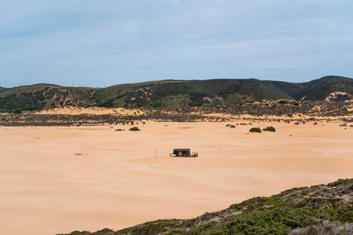 Sand dunes at Praia da Bordeira with wooden surfer hut under blue sky