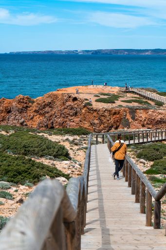 Scenic surf beach Praia da Bordeira with waves rolling in at Algarve Coast with tourist woman standing on boardwalks leading over the sand dunes.