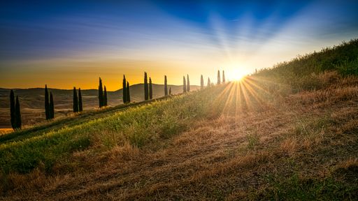 A breathtaking low angle shot of the sunrise in the bright blue sky behind a hill