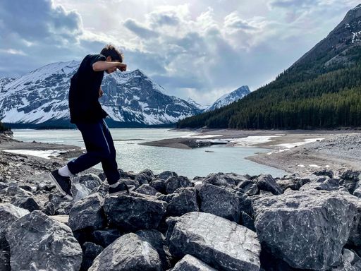 A boy walking on the rocks by a lake with snowy mountains in the background