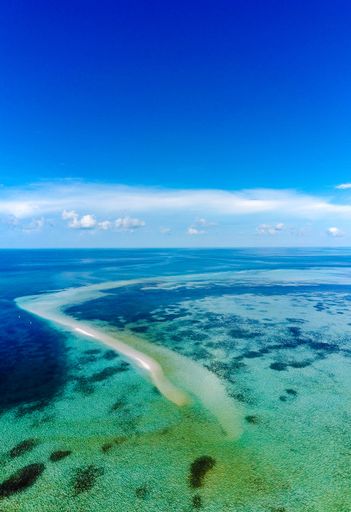 A vertical shot of a white sandbar island in the Bahamas surrounded by a blue ocean