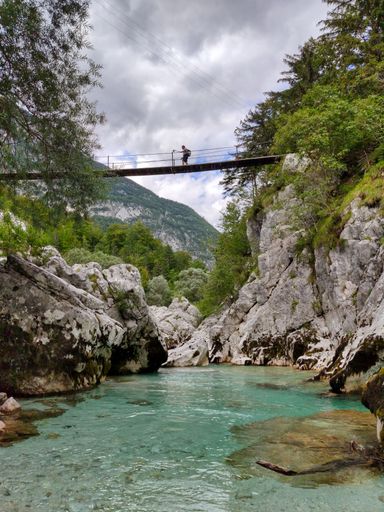A vertical shot of a man walking on a suspension bridge over Soca River in Slovenia