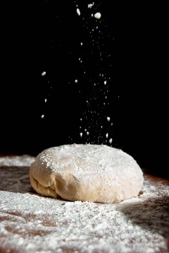 A vertical shot of throwing flour to the pizza dough