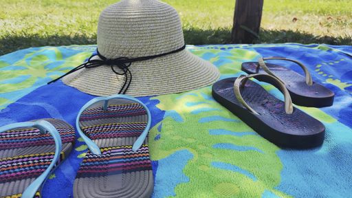 A low angle closeup shot of slippers and a female's straw hat on top of a towel - concept of picnic or summer vacation at the beach