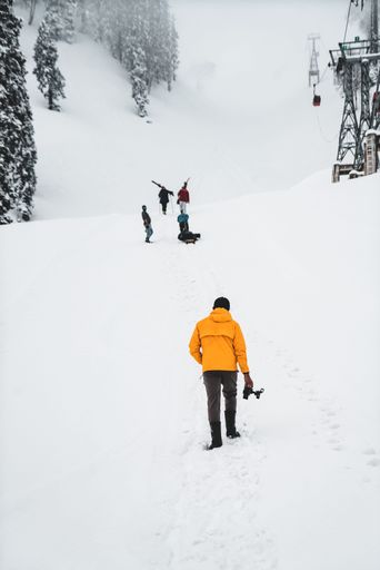 A vertical shot of a photographer in a yellow jacket following a group of children having fun in the snow