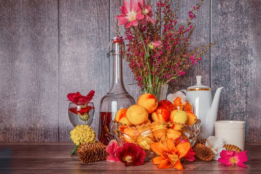 Positive summer still life with bottle of wine bouquet of flowers and ripe peaches in vases wine glasses with mineral water on dark wooden background