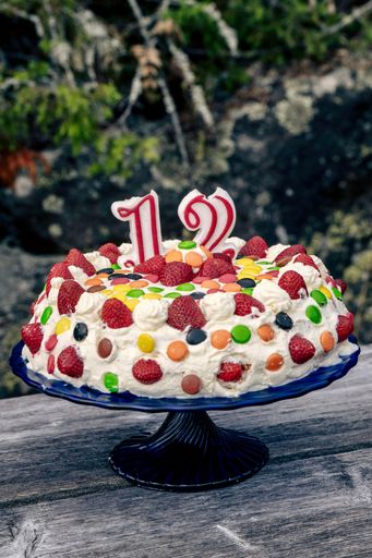 A vertical shot of12 candle on birthday cake decorated with colorful candies and strawberries