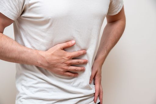 A man, isolated on a blue background, holding his belly with one hand in pain