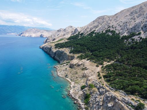 An aerial view of rocky cliffs with green plants by the sea coast in Baska, Croatia