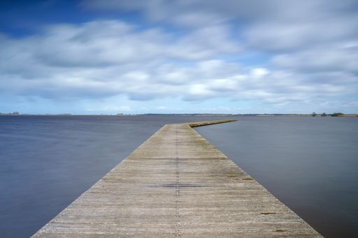 A long wooden pier extending into a beautiful sea under a cloudy blue sky