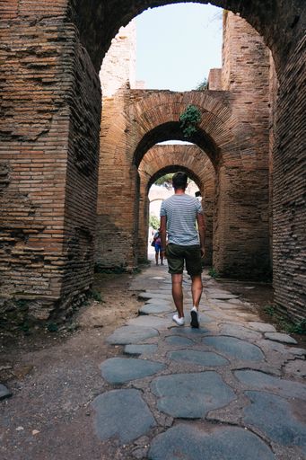 A vertical shot of a person walking in old neighborhoods with triumphal arches during daytime
