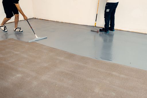 A construction workers applying grey epoxy resin in an industrial hall