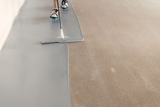 A construction worker applying grey epoxy resin in an industrial hall