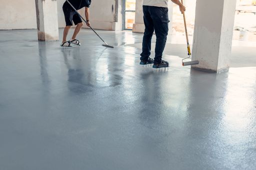 Two construction workers applying grey epoxy resin in an industrial hall
