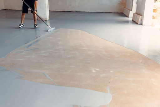 A construction worker applying grey epoxy resin in an industrial hall